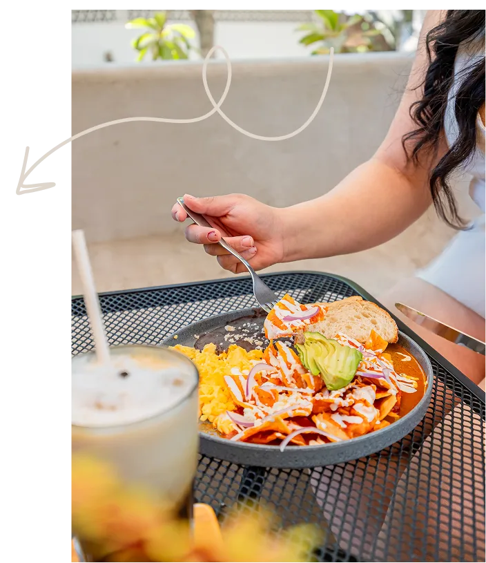Persona disfrutando de un plato de chilaquiles con huevos revueltos y aguacate en una terraza