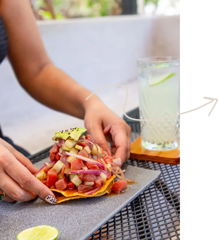 Persona sosteniendo una tostada de atún fresco con aguacate y cebolla morada junto a una bebida refrescante